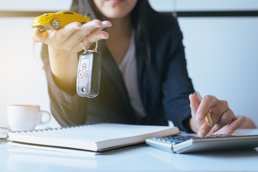 Image of a female loan officer handing a car key and yellow toy car toward the camera.