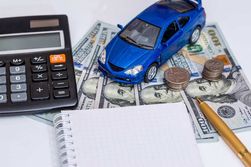 Image of a blue toy car, a pencil, calculator, and note pad sitting on dollar bills.