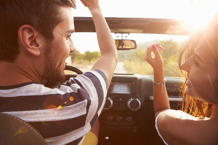Image of a young couple driving into the sunset in a convertible.