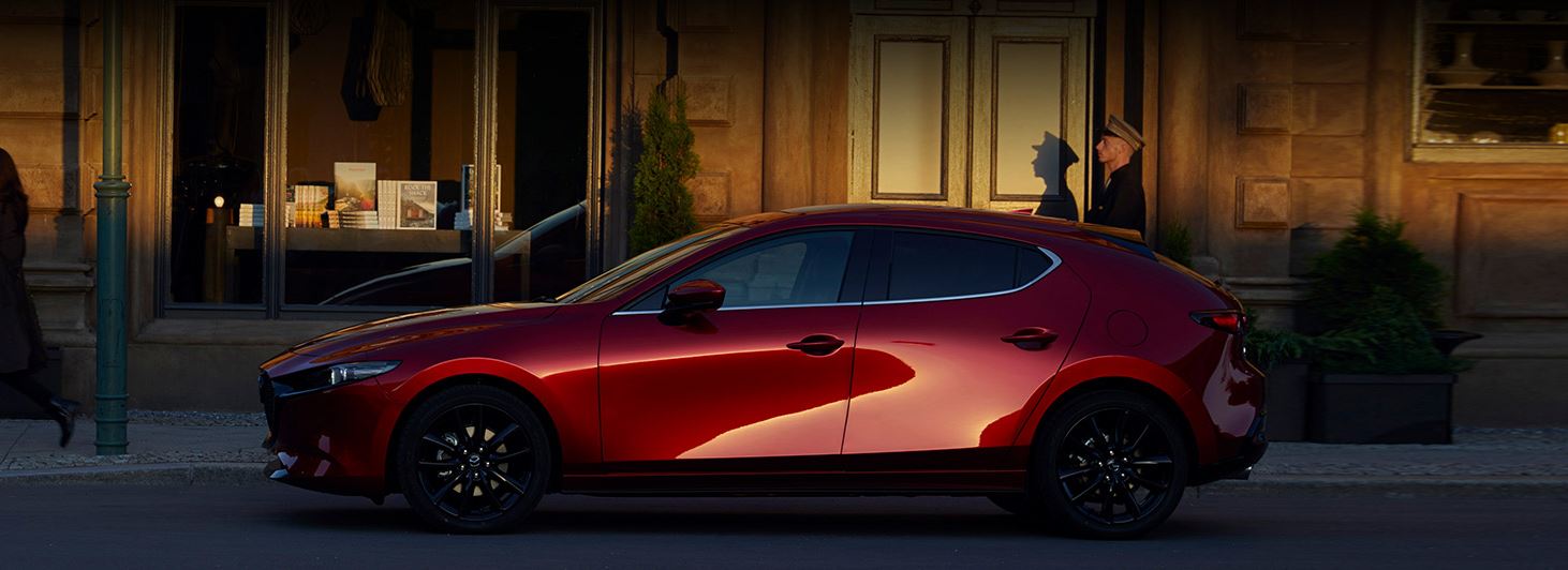 Image of a red 2020 Mazda3 parked in front of a hotel.