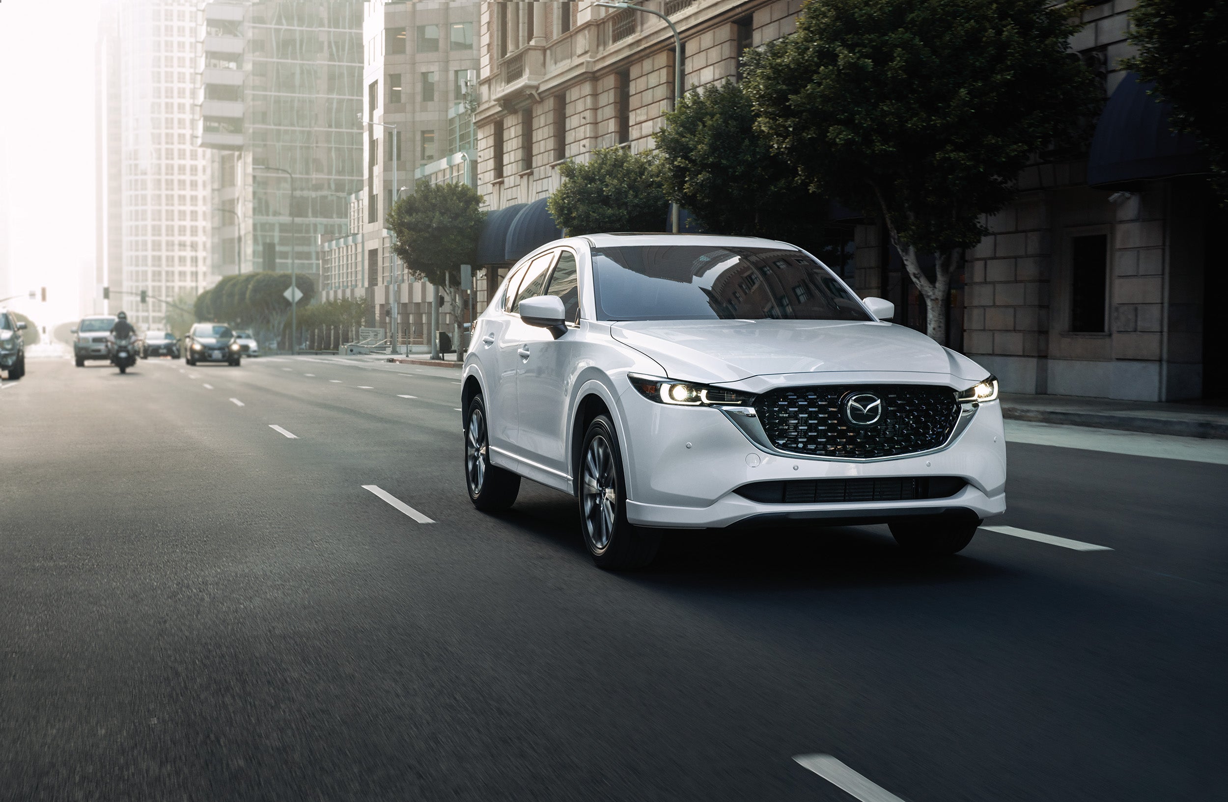 White 2023 Mazda CX-5 drives down street.