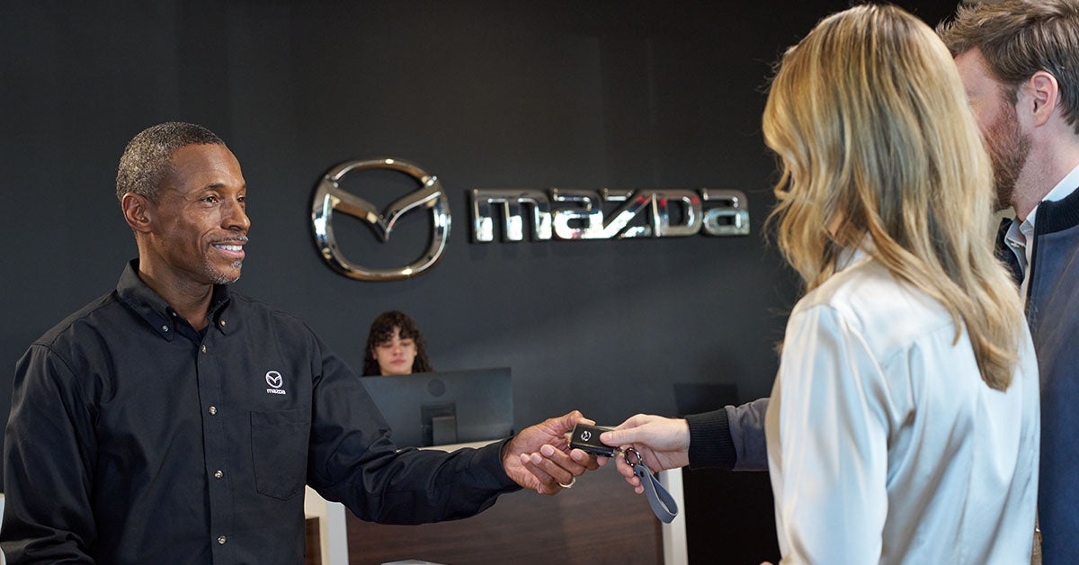 "Mazda dealership employee handing over car keys to a customer at the Peruzzi Mazda service counter,
